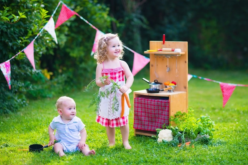 zwei kleine Kinder spielen mit einer Matschküche im Garten