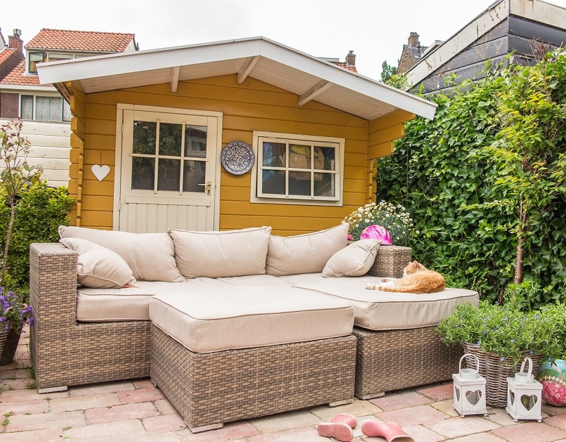 sehr schönes Gartenhaus mit Loungemöbeln davor, eine rote Katze liegt darauf