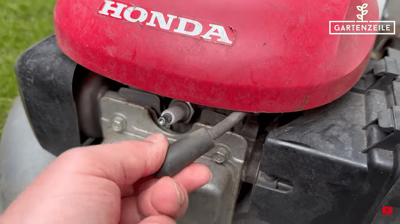 Der Stecker der Zündkerze eines Benzin-Rasenmähers wird entfernt.